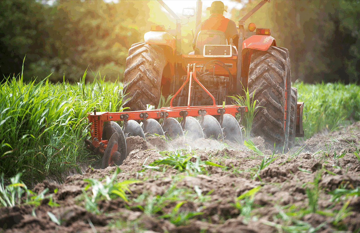 Image of tractor pulling a plough with the sun setting behind.