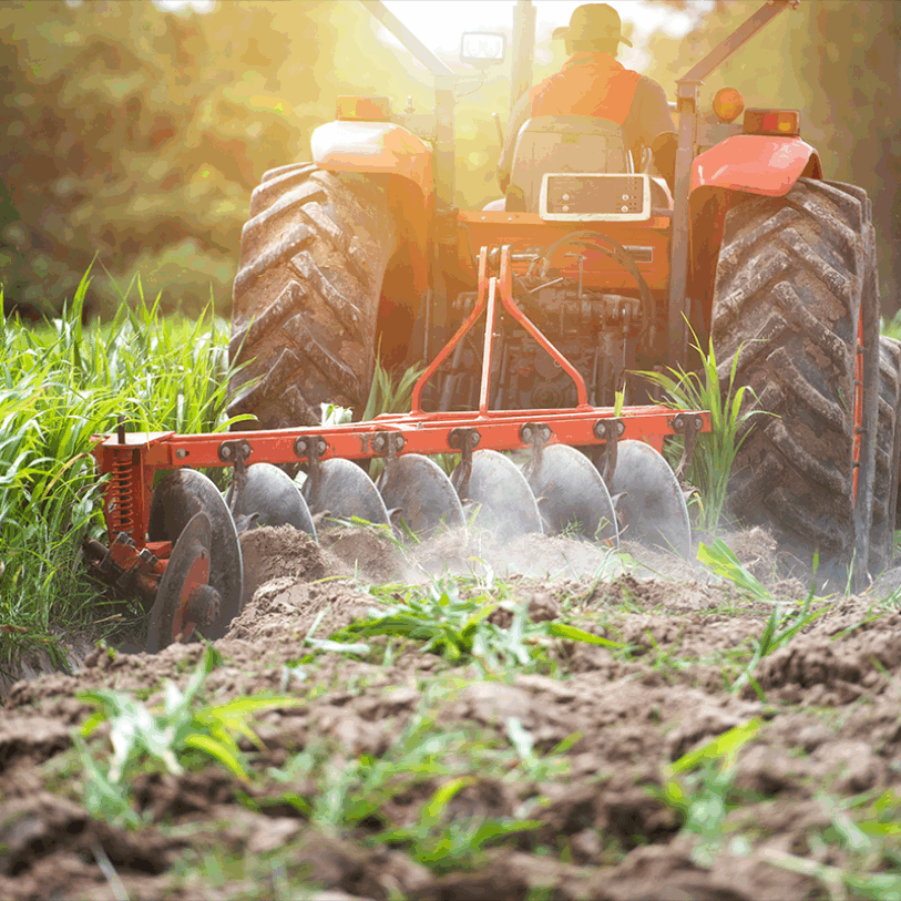 Image of tractor pulling a plough with the sun setting behind.